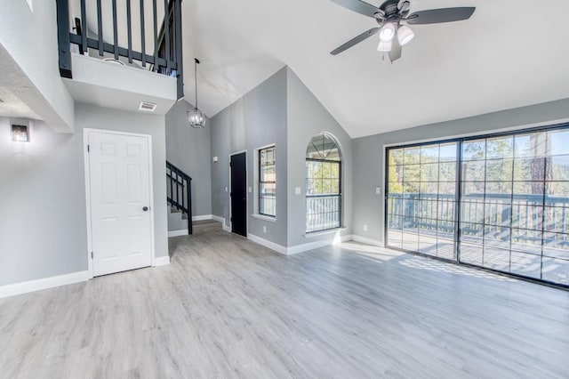 unfurnished living room featuring ceiling fan with notable chandelier, high vaulted ceiling, and light wood-type flooring