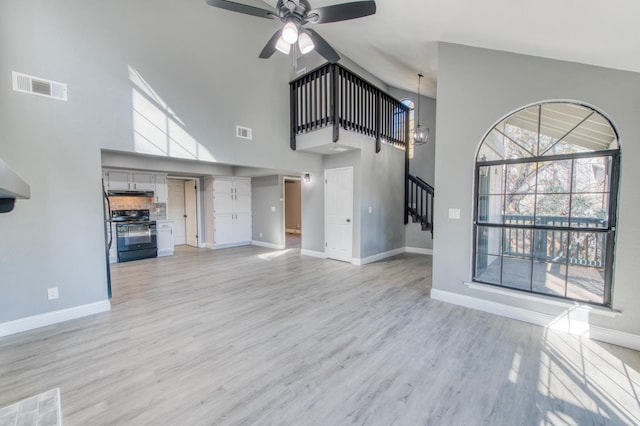 unfurnished living room with ceiling fan with notable chandelier, a high ceiling, and light wood-type flooring