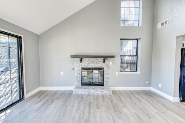 unfurnished living room featuring a brick fireplace, high vaulted ceiling, and light wood-type flooring