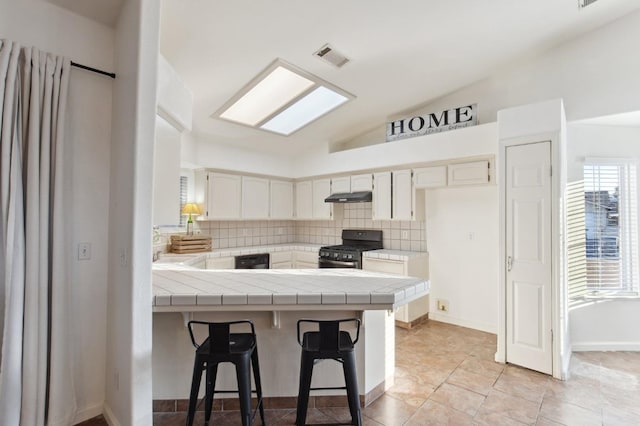 kitchen featuring lofted ceiling, tile countertops, black range with gas stovetop, decorative backsplash, and white cabinets