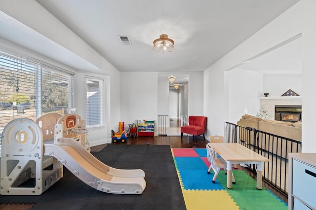 game room with visible vents, baseboards, wood finished floors, and a tile fireplace