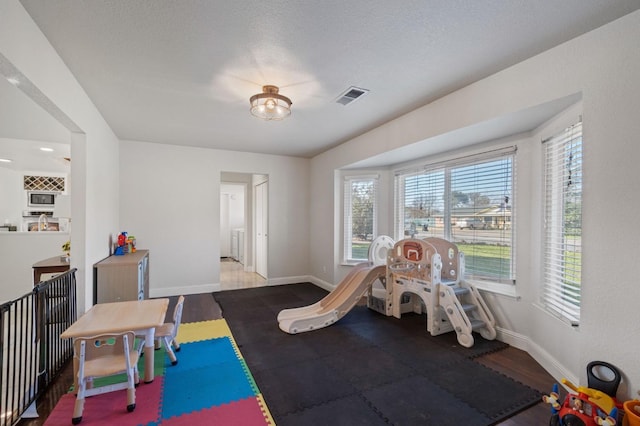 recreation room with visible vents, a textured ceiling, baseboards, and wood finished floors