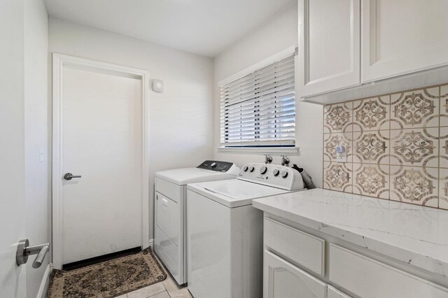 clothes washing area with cabinets, washing machine and clothes dryer, and light tile patterned floors