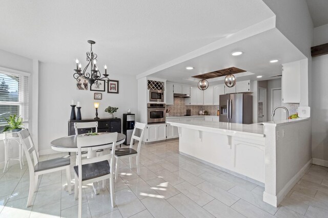 kitchen with appliances with stainless steel finishes, white cabinetry, backsplash, hanging light fixtures, and kitchen peninsula