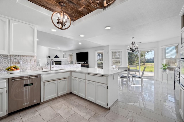 kitchen with an inviting chandelier, a tray ceiling, a fireplace, a sink, and appliances with stainless steel finishes