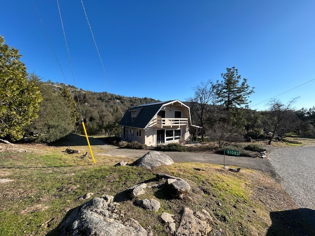 view of front facade with a gambrel roof, a wooded view, and a balcony