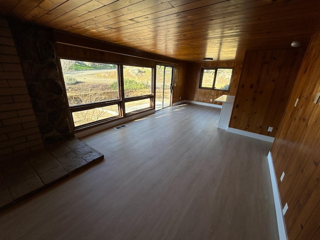 unfurnished living room featuring wood finished floors, visible vents, baseboards, wood walls, and wooden ceiling