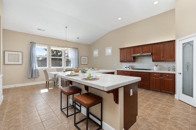 kitchen with pendant lighting, tasteful backsplash, lofted ceiling, a center island, and tile counters