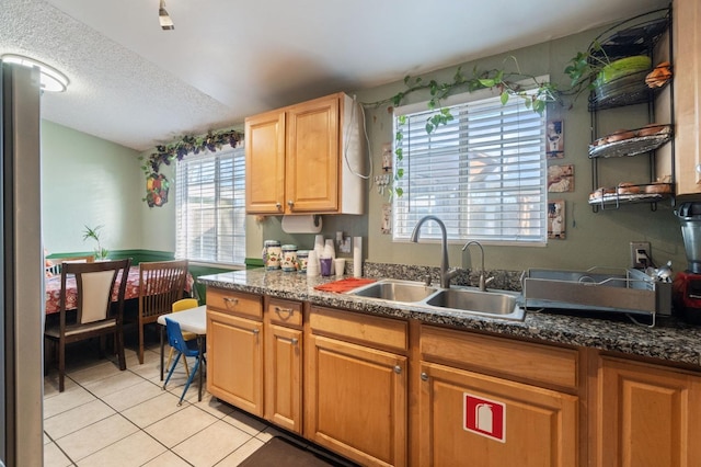 kitchen with sink, stainless steel refrigerator, a textured ceiling, light tile patterned flooring, and dark stone counters