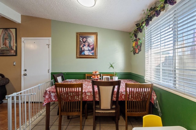 dining space featuring tile patterned flooring, vaulted ceiling, and a textured ceiling