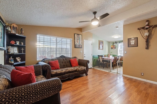 living room with vaulted ceiling, ceiling fan, a textured ceiling, and light wood-type flooring