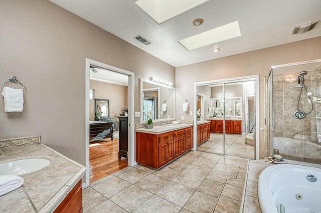 full bathroom with a skylight, two vanities, visible vents, a stall shower, and a sink