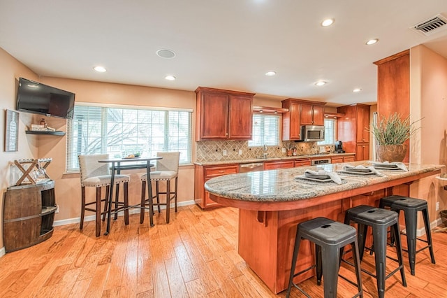 kitchen featuring visible vents, a kitchen breakfast bar, appliances with stainless steel finishes, decorative backsplash, and light wood finished floors