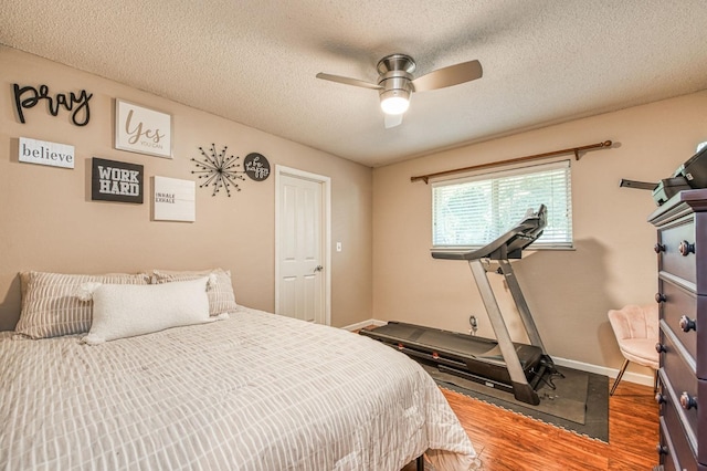 bedroom featuring ceiling fan, a textured ceiling, baseboards, and wood finished floors