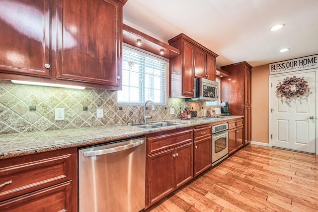 kitchen featuring light stone counters, a sink, appliances with stainless steel finishes, light wood-type flooring, and backsplash