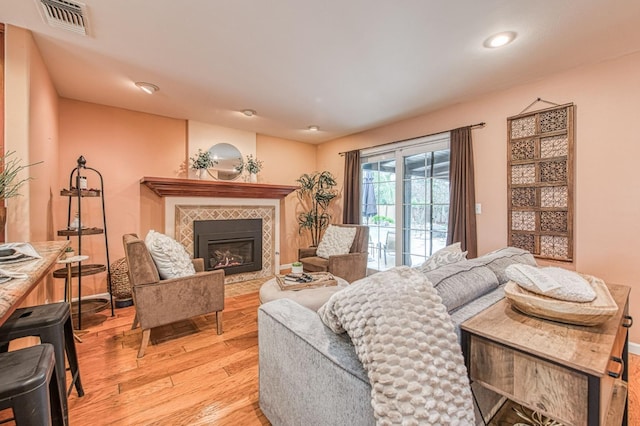 living room with light wood finished floors, a tiled fireplace, visible vents, and baseboards