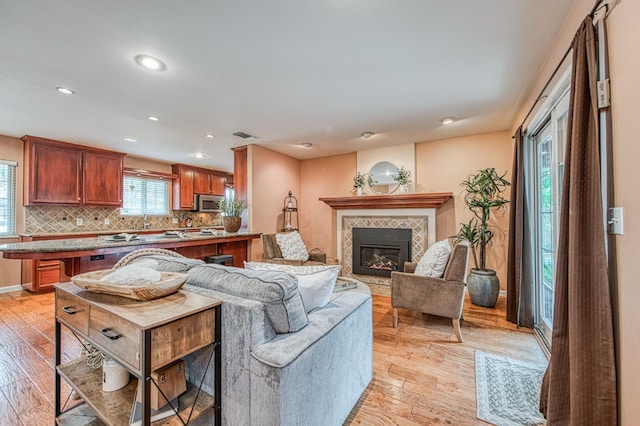 living area with recessed lighting, visible vents, light wood-style flooring, a tiled fireplace, and baseboards