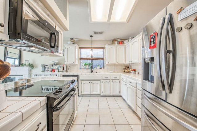 kitchen featuring range with two ovens, stainless steel refrigerator with ice dispenser, tile countertops, light tile patterned floors, and black microwave