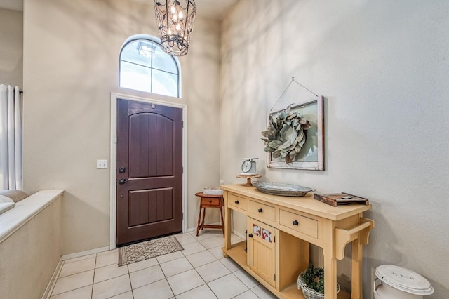 foyer with light tile patterned floors, a high ceiling, baseboards, and a chandelier