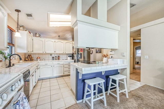 kitchen featuring light tile patterned flooring, a sink, visible vents, tile counters, and stainless steel fridge with ice dispenser