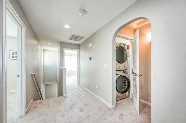 hall with stacked washing maching and dryer and light colored carpet