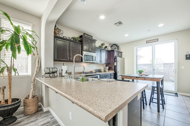 kitchen featuring a breakfast bar, sink, dark brown cabinetry, kitchen peninsula, and stainless steel appliances