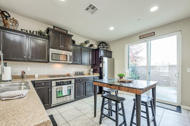 kitchen featuring dark brown cabinetry, light tile patterned floors, stainless steel appliances, and sink