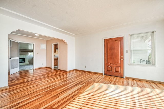 spare room with a brick fireplace, a textured ceiling, and light hardwood / wood-style flooring