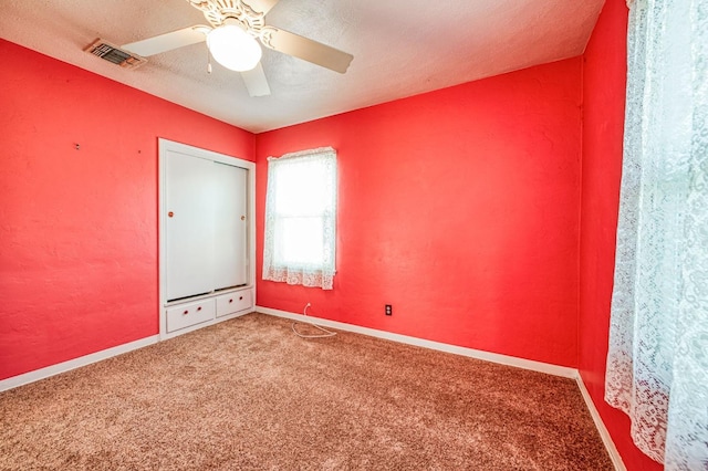 carpeted empty room with ceiling fan and a textured ceiling