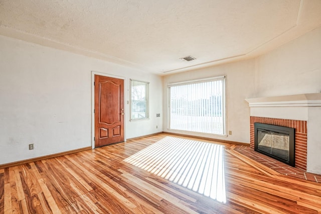 unfurnished living room with a brick fireplace, a textured ceiling, and light hardwood / wood-style floors