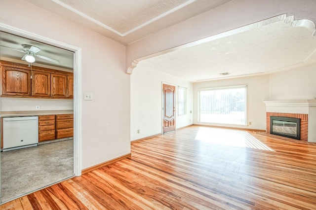 unfurnished living room featuring ceiling fan, a textured ceiling, a fireplace, and light hardwood / wood-style floors