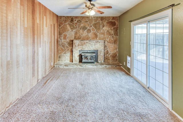 unfurnished living room featuring a wood stove, carpet, ceiling fan, and wood walls