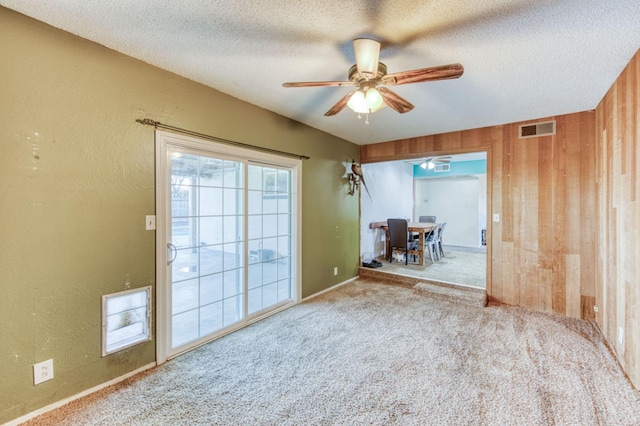 unfurnished room with ceiling fan, light carpet, a textured ceiling, and wooden walls