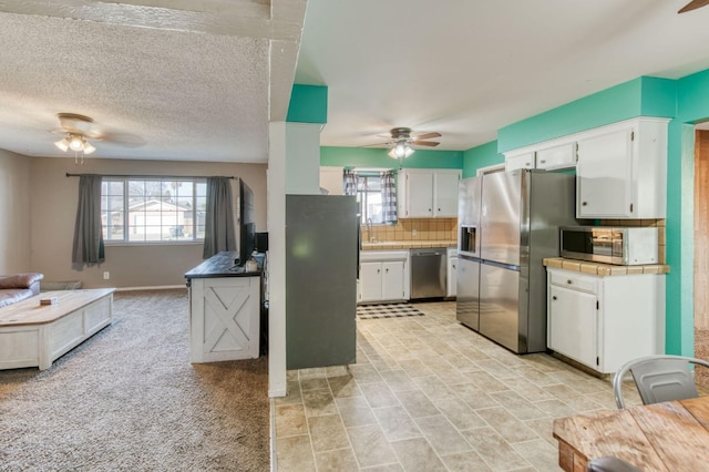 kitchen featuring a textured ceiling, white cabinets, ceiling fan, stainless steel appliances, and backsplash