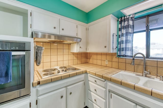 kitchen featuring cooktop, stainless steel oven, tile counters, decorative backsplash, and white cabinets