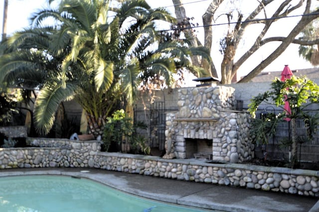 view of swimming pool featuring a fenced in pool and an outdoor stone fireplace