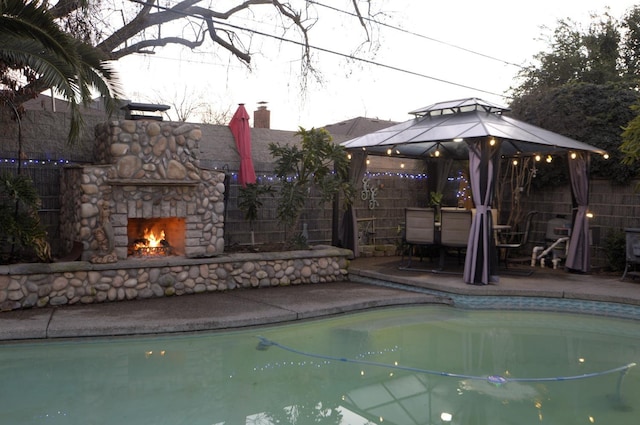 pool featuring a gazebo, a patio, an outdoor stone fireplace, and fence