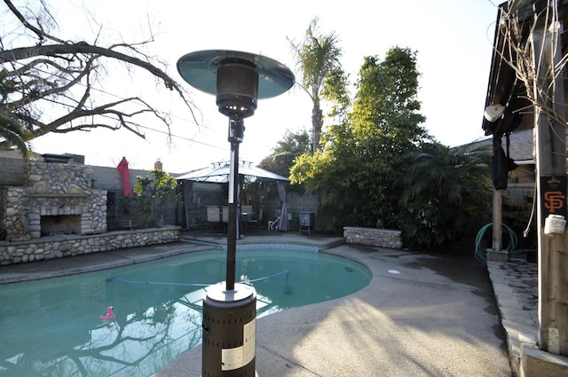 view of swimming pool with a gazebo, a fenced in pool, a patio, and an outdoor stone fireplace