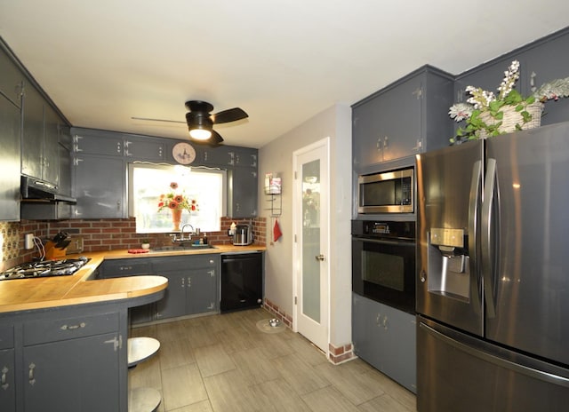 kitchen featuring tasteful backsplash, under cabinet range hood, light countertops, black appliances, and a sink