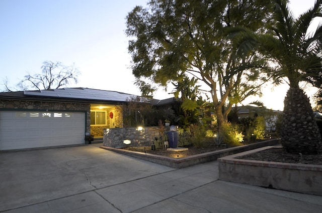 single story home with a garage, roof mounted solar panels, and concrete driveway