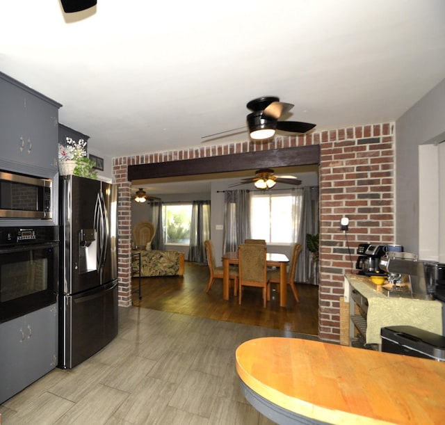 kitchen featuring light wood-style flooring, black oven, ceiling fan, stainless steel microwave, and fridge with ice dispenser