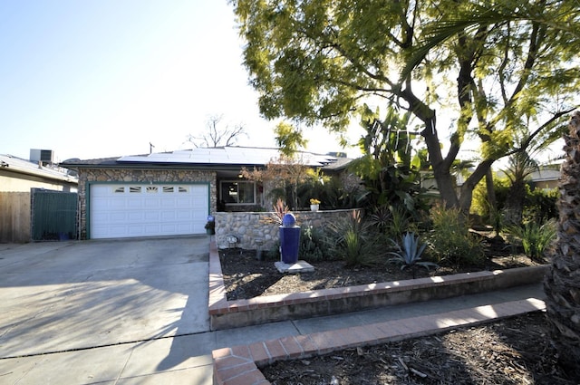 single story home featuring stone siding, roof mounted solar panels, fence, concrete driveway, and a garage