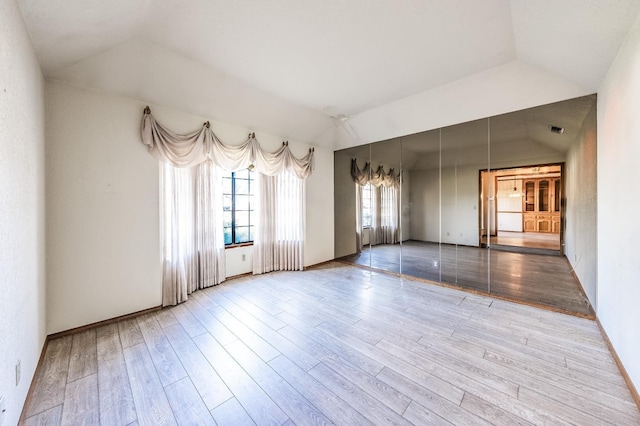 unfurnished room with lofted ceiling, a tray ceiling, and light hardwood / wood-style flooring