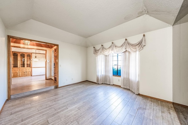 empty room featuring lofted ceiling, a tray ceiling, light hardwood / wood-style flooring, and a textured ceiling