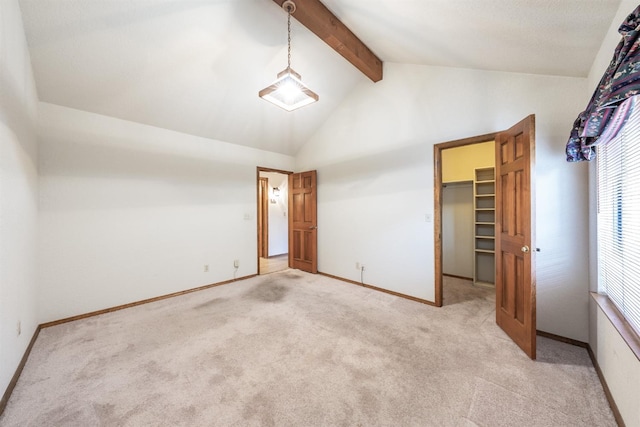 unfurnished bedroom featuring light carpet, a walk in closet, lofted ceiling with beams, and a closet