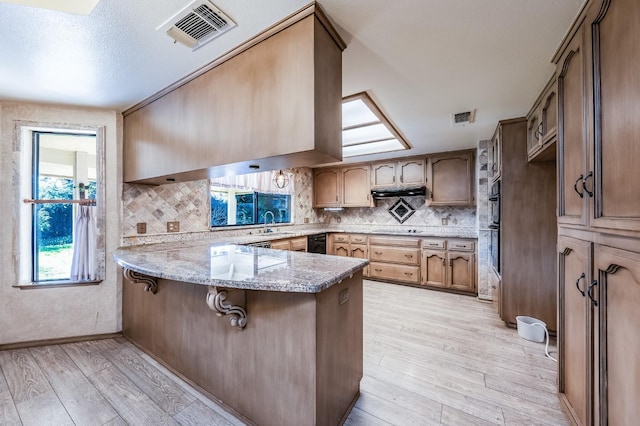 kitchen featuring light hardwood / wood-style flooring, a kitchen breakfast bar, light stone countertops, decorative backsplash, and kitchen peninsula