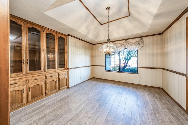 unfurnished dining area featuring an inviting chandelier, a tray ceiling, crown molding, and light wood-type flooring