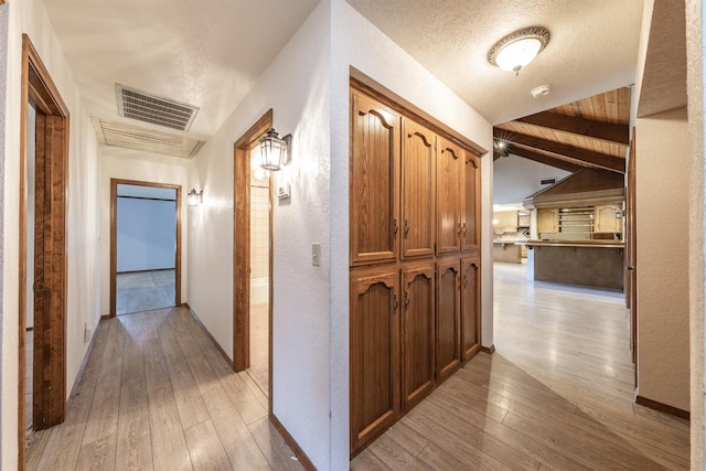 corridor with vaulted ceiling with beams, a textured ceiling, wooden ceiling, and light wood-type flooring