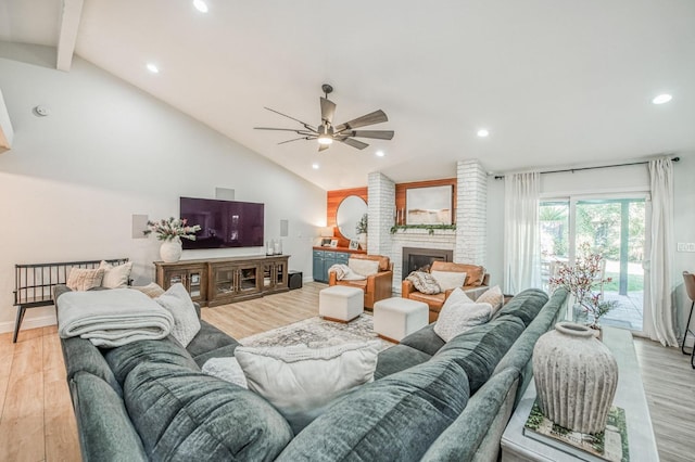 living room featuring ceiling fan, high vaulted ceiling, light hardwood / wood-style floors, a brick fireplace, and beamed ceiling