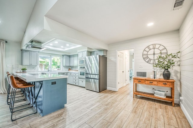 kitchen featuring appliances with stainless steel finishes, kitchen peninsula, light hardwood / wood-style flooring, and wood walls